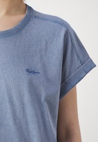 Tricou cu mânecă scurtă de culoare albastru deschis, confecționat din bumbac moale. Are un guler rotund și un logo brodat discret pe piept.