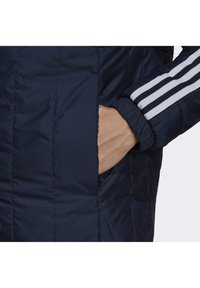 Tmavě modrá prošívaná bunda s boční kapsou, vyrobená z texturovaného materiálu a s bílými proužky na manžetě.