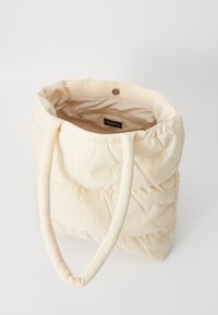 Sac fourre-tout matelassé crème en tissu doux, doté de deux poignées et d'une poche intérieure zippée. Léger avec une forme structurée.