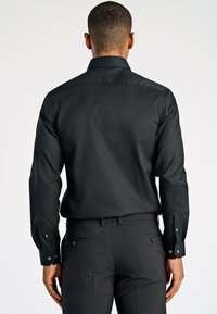 Zwart overhemd met lange mouwen, slim fit ontwerp en knoopmanchetten, gecombineerd met donkere broeken. Gladde textuur en klassieke kraag.