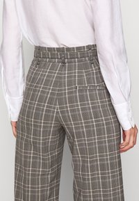 Grå rutiga byxor med hög midja, i en texturerad tygkvalitet, vida ben och en detalj med bakficka. Matchat med en vit långärmad skjorta.