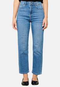 Jeans de tiro alto en azul claro, de pierna recta, con cinco bolsillos, costuras sutiles y dobladillo sin terminar, combinados con bailarinas patentadas negras.