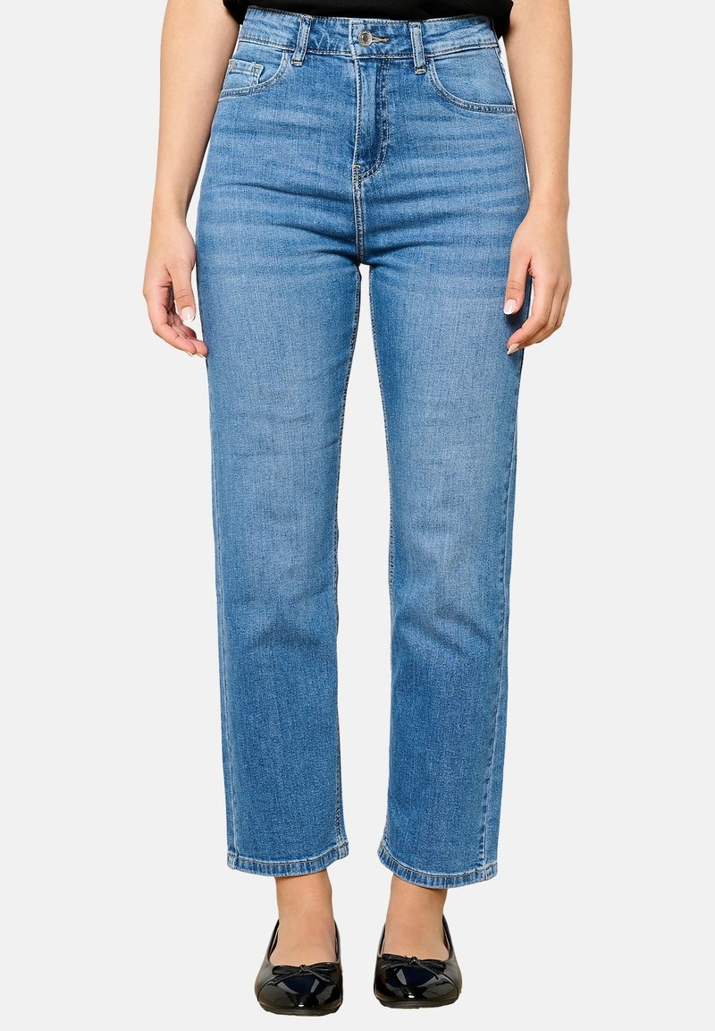 Jeans de tiro alto en azul claro, de pierna recta, con cinco bolsillos, costuras sutiles y dobladillo sin terminar, combinados con bailarinas patentadas negras.