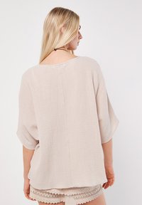 Ljusbeige, strukturerad blus med lös passform, delad rygg och korta ärmar. Tillverkad av ett mjukt, andningsbart tyg med ett subtilt mönster.