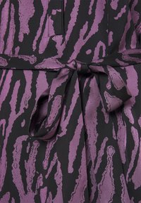 Svart tyg med ett lila abstrakt djurtryck, prydt med ett knytbälte i midjan. Materialet har en slät yta.