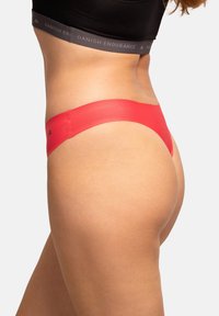 String rouge en tissu lisse et extensible. Il possède une taille fine et une couverture minimale. Aucun motif visible ni détail matériel.