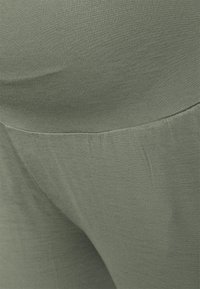 Tecido canelado verde-azeitona em close-up de leggings, mostrando uma textura suave com um leve elasticidade e um acabamento limpo na cintura.