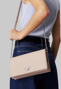 Borsa a tracolla in pelle rosa chiaro con tracolla a catena, design pieghevole e un accento con logo argentato. Texture liscia, forma rettangolare.