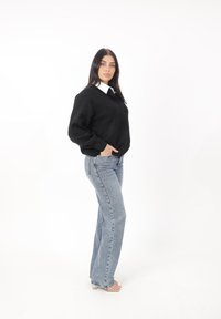 Maglione nero a maglia con una camicia bianca colletto sotto, abbinato a jeans a gamba larga blu chiaro e sandali con tacco trasparenti.