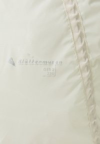 Lett, off-white stoff med en jevn tekstur. Har en sydd kant og trykt logo med "Gebo 23L" i sølv. Minimalistisk design.