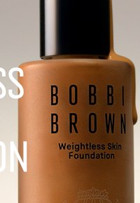 Bobbi Brown Weightless Skin Foundation i en matt, ljusbrun flaska med ett svart lock; etiketten har fet svart text på en slät yta.