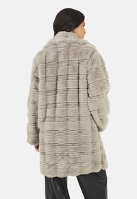 Jasnoszary płaszcz z futra syntetycznego o fakturowanym, prążkowanym wzorze. Posiada wycięty kołnierz i luźny krój, sięgający poniżej bioder.