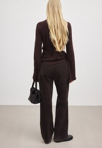 Dunkelbraune, weiche Wildleder- Schlaghosen mit Gesäßtaschen, kombiniert mit einem taillierten dunklen Pullover und einer kleinen schwarzen Handtasche. Glatte Textur.