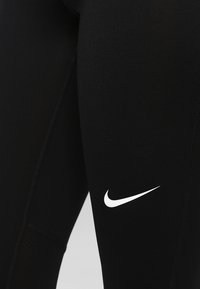 Leggings sportivi neri realizzati in materiale elasticizzato, con un piccolo logo Nike bianco sulla coscia e una texture liscia e slanciata.