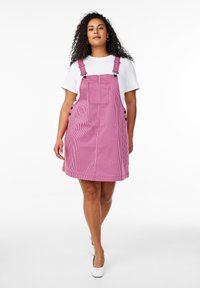Vestido de denim a rayas rosas y blancas con tirantes, bolsillo frontal y detalles de botones a los lados. Combinado con una camiseta blanca debajo.