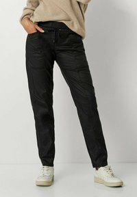 Schwarze, elastische Hosen mit einem glatten Material, ausgestattet mit Seitentaschen, einem Kordelzug und einem schmal zulaufenden Bein Design.