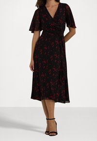 Svart omlottklänning med korta volangärmar, prydd med små röda blommönster. Slät textur, knälång, knuten i midjan.