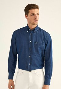 Camicia in denim blu scuro con maniche lunghe, colletto a punte e tasca sul petto. Presenta bottoni bianchi e un tessuto texturizzato.