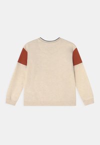 Suéter beige con mangas largas, cuello redondo y parches en los hombros de color marrón contrastante. Textura suave con puños y dobladillo acanalados.