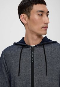 Kapuzensweatshirt mit Reißverschluss in Dunkelblau aus strukturiertem Stoff, mit einem Logo am Reißverschluss und schwarzen Kordeln.