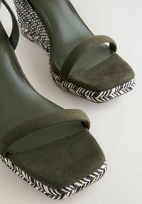 Sandali con tacco a cuneo in suede verde oliva, con punta quadrata e decorazioni in tessuto intrecciato bianco e nero sul tacco.