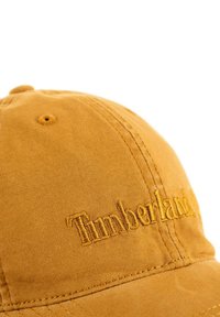Brown cotton baseball cap with embroidered "Timberland" logo in yellow, featuring stitched accents and a curved brim.