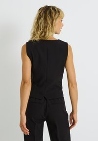 Haut noir sans manches, ajusté et cintré, avec un détail subtil de couture au dos, fabriqué en tissu lisse.