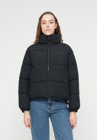 Μαύρο μπουφάν puffer με ψηλό γιακά, κλείσιμο με φερμουάρ και ριμπ μανσέτες. Διαθέτει σχεδιασμό με ραφές και λογότυπο στο στήθος.