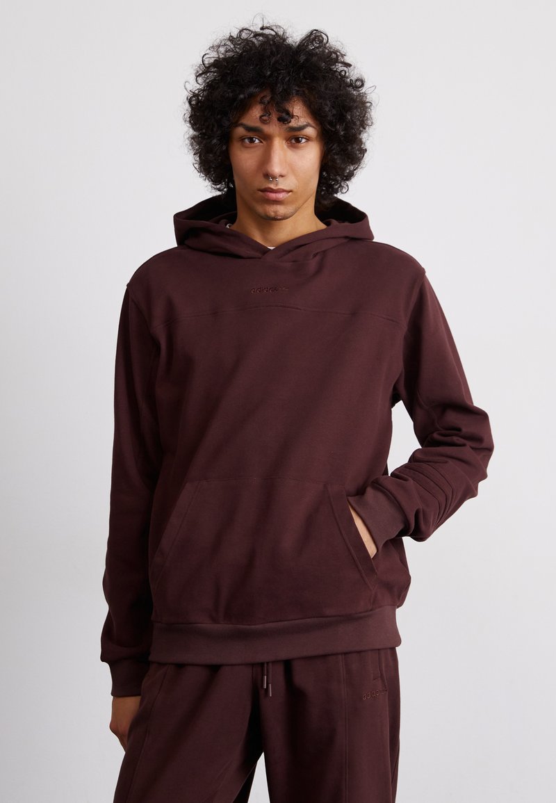 Felpa maroon con tasca a kangaroo e cappuccio regolabile con cordini. Realizzata in tessuto morbido, presenta un logo sottile sul petto, polsini e orlo a costine.