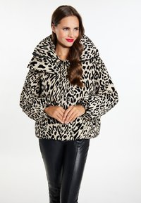 Gevoerde leopardprintjas in beige en zwart, met een brede kraag, elastische manchetten en een boxy silhouet. Geplaatst tegen een effen achtergrond.