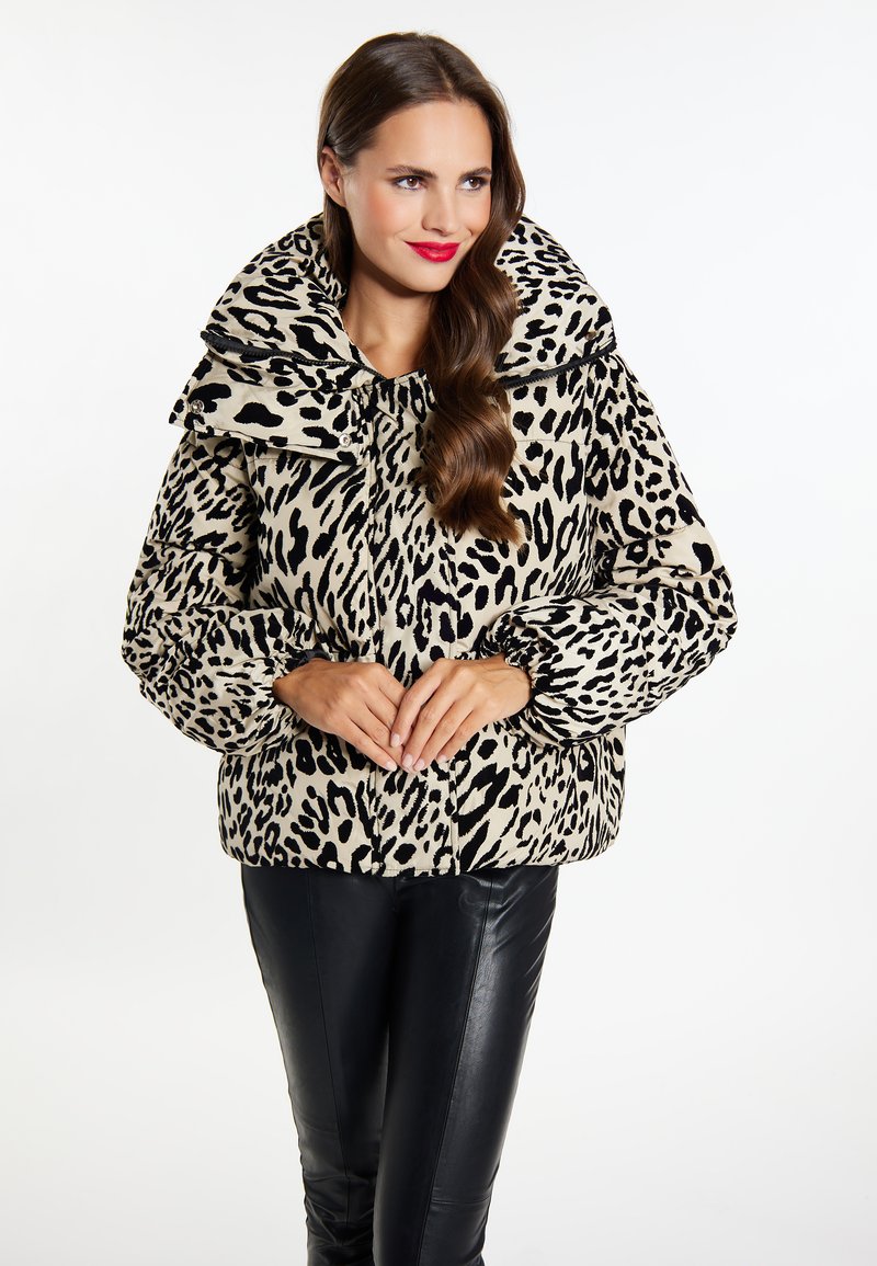 Gevoerde leopardprintjas in beige en zwart, met een brede kraag, elastische manchetten en een boxy silhouet. Geplaatst tegen een effen achtergrond.
