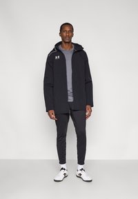 Μαύρο ελαφρύ μπουφάν με κλείσιμο με φερμουάρ, γκρι πολυεπίπεδο πουκάμισο και μαύρο παντελόνι. Λευκά αθλητικά παπούτσια με μαύρες λεπτομέρειες. Απλός σχεδιασμός, λειτουργικό στυλ.