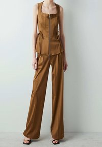 Completo marrone a due pezzi composto da un top aderente con zip e scollatura quadrata, arricchito da dettagli con coulisse, abbinato a pantaloni a gamba larga.