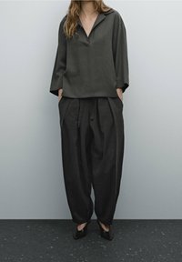 Chemise ample gris foncé avec col, complétée par un pantalon larges assorti. Le matériau semble texturé avec un éclat subtil.