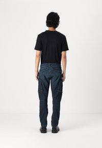 Dark blue cargo pants made from denim, featuring side pockets, a slim fit, and a mid-rise waist. Paired with a black short-sleeve shirt.