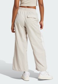 Ανοιχτό μπεζ παντελόνι σε ίσια γραμμή με υφή και ελαφρύ ύφασμα, διαθέτει λευκές λωρίδες στα πλάγια και πίσω τσέπη. Φοριέται με λευκά αθλητικά παπούτσια.