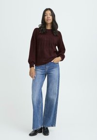 Maglione bordeaux lavorato a maglia con texture a coste e maniche a palloncino, abbinato a jeans a gamba larga azzurri e stivaletti neri.