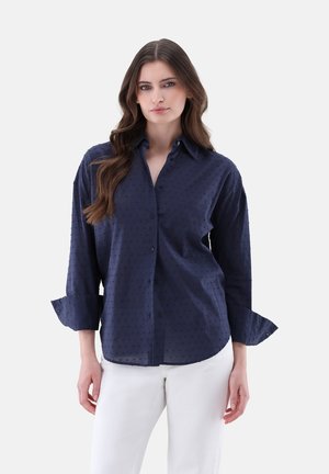 Camicia blu navy a bottoni con un motivo testurizzato, maniche lunghe arrotolate ai polsi e colletto classico. Tessuto morbido. Vestibilità sagomata.