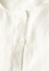 Blusa bianca in lino con scollatura rotonda, quattro bottoni sul davanti e un tessuto strutturato con una finitura morbida e naturale.