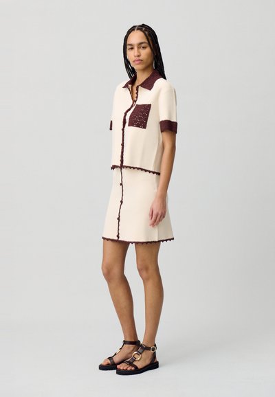 Completo crema a due pezzi composto da una cropped button-up con taschino bordeaux e gonna abbinata, entrambi con rifiniture testurizzate e maniche corte.
