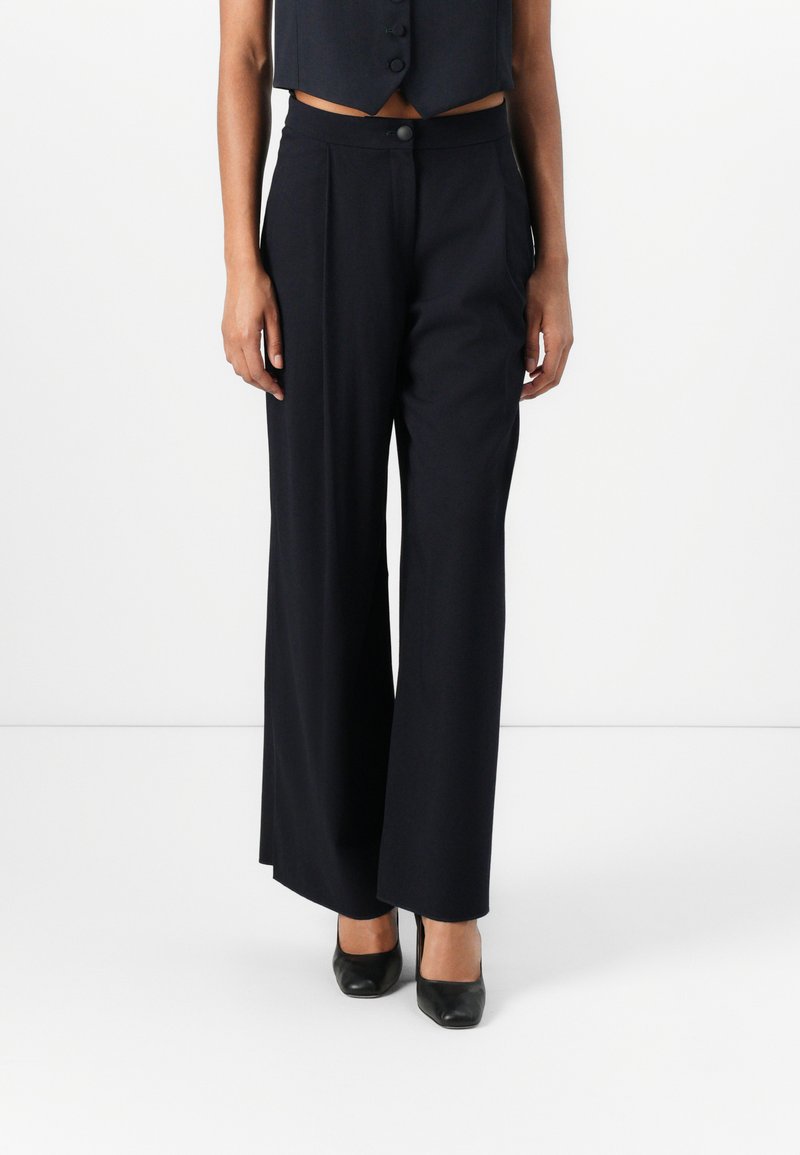 Brede, marineblauwe broek van een gladde stof. Beschikt over een knoopsluiting, zijzakken en een op maat gemaakte pasvorm.