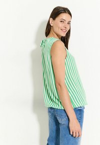 Grön och vit randig ärmlös topp med en rosett på ryggen, kombinerad med blå denimjeans som har en avslappnad passform.