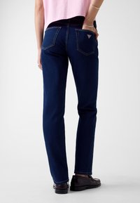 Granatowe dżinsy z denimu o prostym kroju nogawki, pięcioma kieszeniami i trójkątnym logo na tylnej kieszeni. Gładka faktura, klasyczny design.