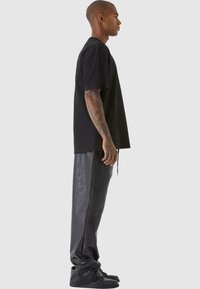 Svart kortermet t-skjorte kombinert med skinnende svarte faux skinnbukser. Modellen står på siden og viser frem den avslappede passformen og enkle designet.