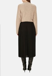 Un pull en tricot beige associé à une jupe midi plissée noire. La tenue offre une coupe décontractée et une texture douce. Des bottes noires montantes complètent le look.