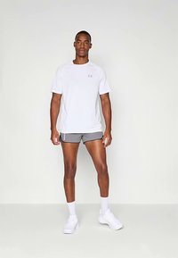 Λευκό αθλητικό μπλουζάκι με κοντά μανίκια και γκρι λογότυπο, συνδυασμένο με γκρι σορτς και λευκά αθλητικά παπούτσια, σε απλό φόντο.