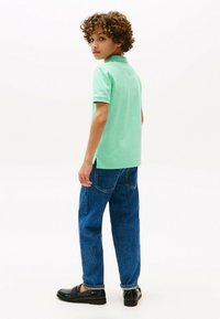 Polo shirt verde menta, jeans in denim blu e scarpe slip-on nere. La shirt ha un colletto e maniche corte, con spacchetti laterali all'orlo.