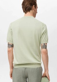 Pulover scurt cu mânecă scurtă, de culoare verde deschis, realizat dintr-un material tricotat moale. Are guler rotund, manșete și tiv cu nervuri, cu o textură fină și o croială lejeră.
