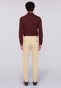 Burgundowa koszula polo z długim rękawem w połączeniu z beżowymi spodniami slim fit, wykonanymi z teksturowanej tkaniny i wyposażonymi w dwie tylne kieszenie z guzikami.