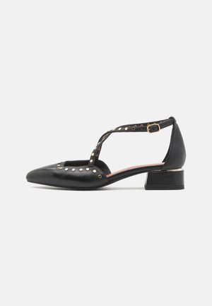 Zapatos de tacón de cuero negro con punta afilada, que cuentan con tachuelas doradas en la correa y un tacón bajo y cuadrado. Correa en el tobillo ajustable para un mejor ajuste.